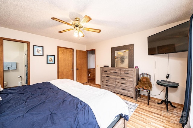 bedroom featuring baseboards, ensuite bath, ceiling fan, a textured ceiling, and light wood-type flooring