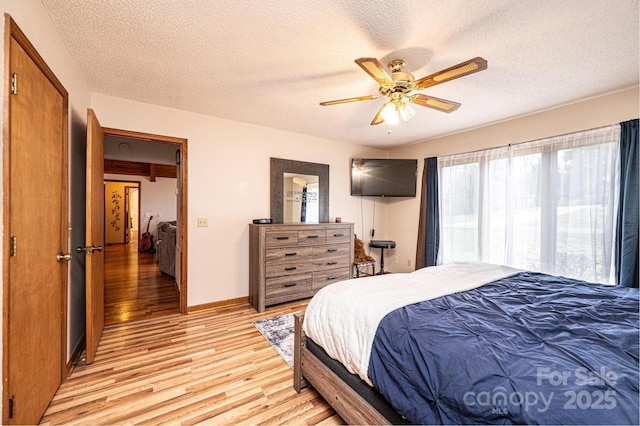 bedroom featuring light wood-style flooring, a ceiling fan, baseboards, and a textured ceiling