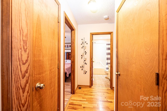 corridor with light wood finished floors, a textured ceiling, and baseboards