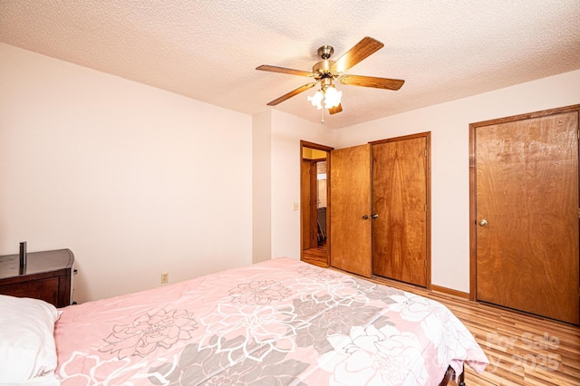 bedroom with a textured ceiling, two closets, ceiling fan, and wood finished floors