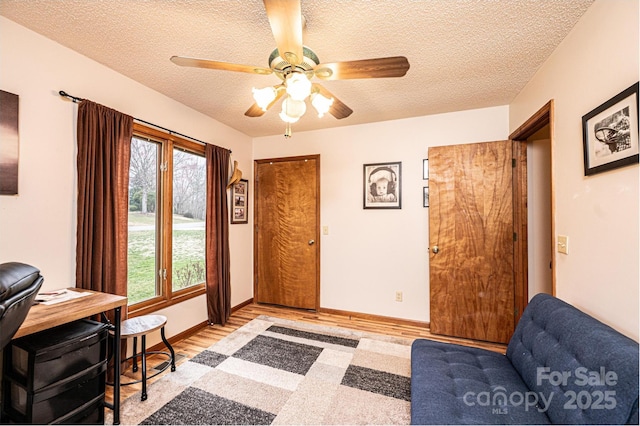 office area featuring a ceiling fan, light wood-style floors, baseboards, and a textured ceiling