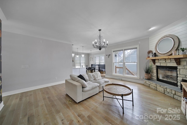 living room with a chandelier, light wood-style flooring, a fireplace, baseboards, and ornamental molding