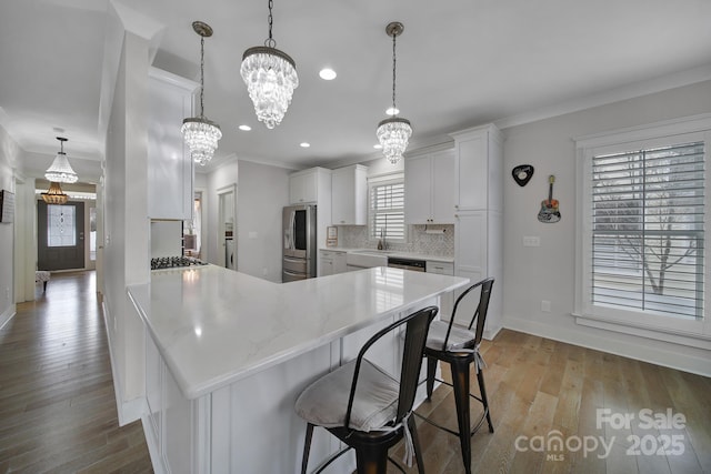 kitchen featuring stainless steel appliances, a peninsula, white cabinets, a kitchen breakfast bar, and backsplash