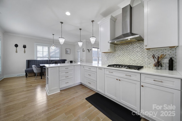 kitchen featuring ornamental molding, a peninsula, wall chimney range hood, stainless steel gas stovetop, and backsplash