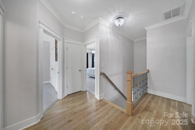 hallway featuring baseboards, visible vents, ornamental molding, wood finished floors, and an upstairs landing