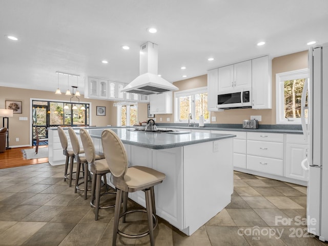 kitchen featuring a kitchen bar, island exhaust hood, a center island, white cabinetry, and white appliances