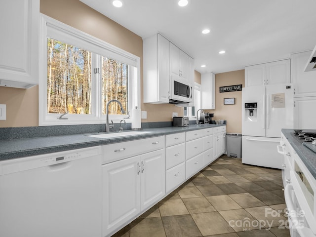 kitchen with white appliances, white cabinets, dark countertops, and a sink