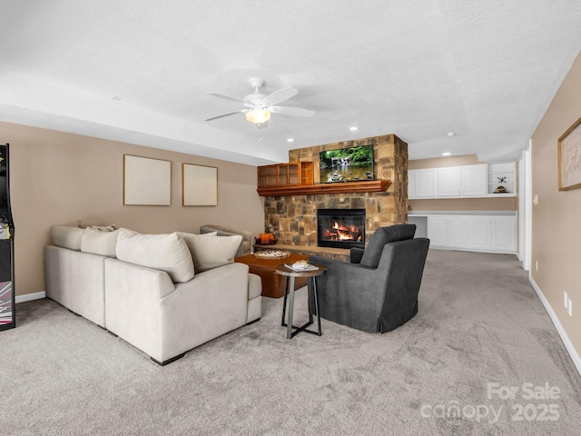 living area with baseboards, light carpet, a fireplace, a textured ceiling, and a ceiling fan