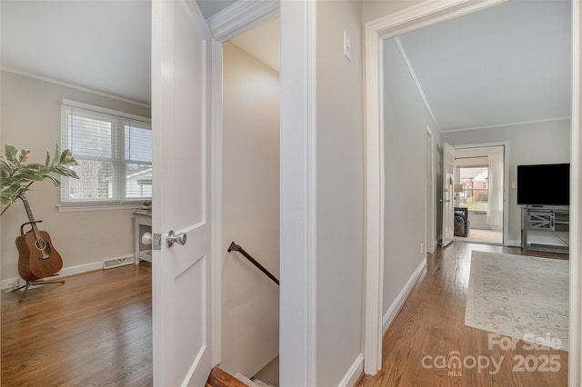 corridor with visible vents, an upstairs landing, wood finished floors, crown molding, and baseboards