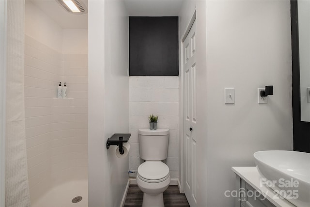 bathroom with vanity, wood finished floors, a shower stall, tile walls, and toilet