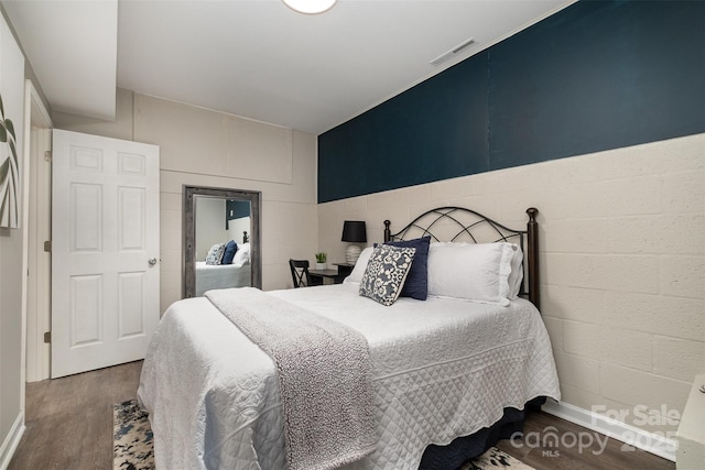 bedroom featuring concrete block wall, wood finished floors, and visible vents