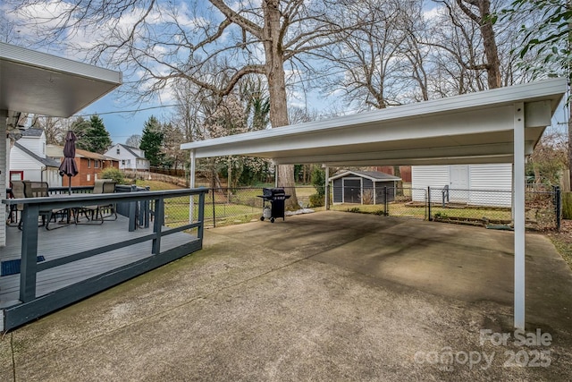 view of parking featuring a detached carport, a storage unit, fence, and driveway