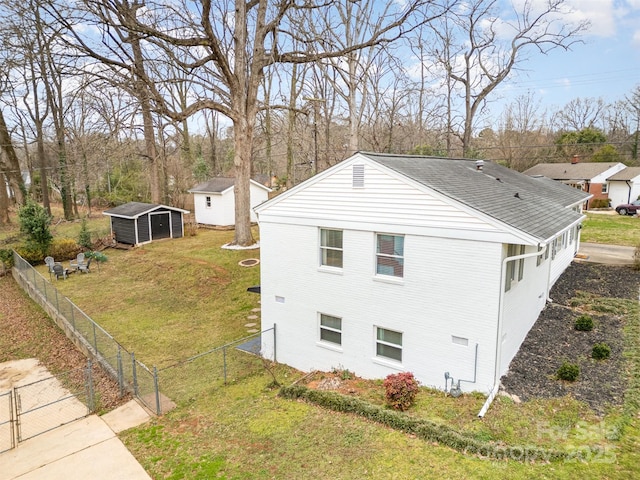 view of property exterior with brick siding, fence private yard, a yard, an outbuilding, and a gate