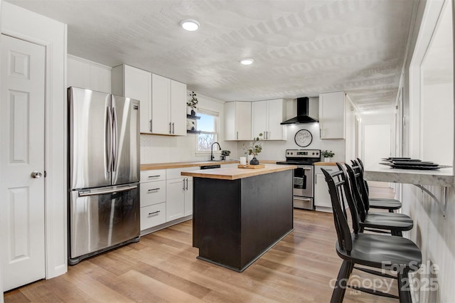 kitchen with stainless steel appliances, light wood-style floors, white cabinets, butcher block countertops, and wall chimney exhaust hood