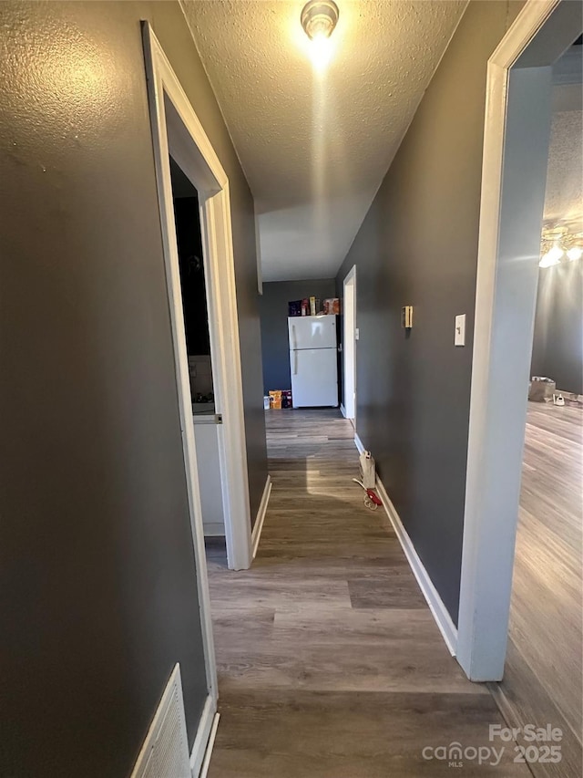 corridor featuring visible vents, a textured ceiling, baseboards, and wood finished floors