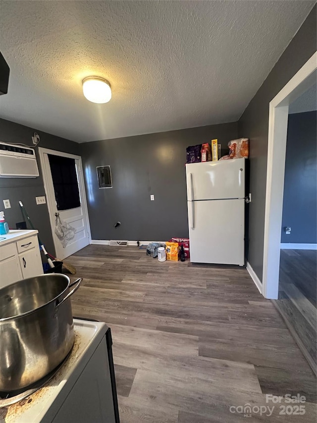 kitchen featuring range, white cabinets, dark wood-type flooring, freestanding refrigerator, and an AC wall unit