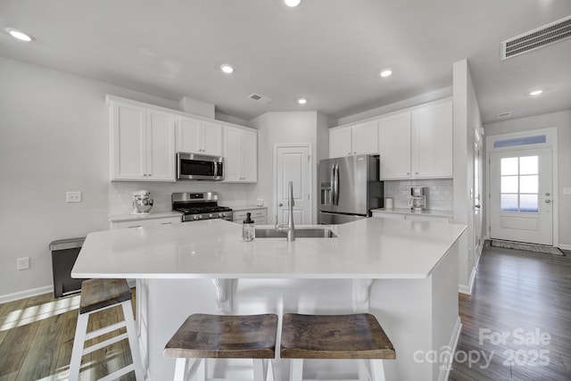 kitchen with a sink, stainless steel appliances, visible vents, and dark wood finished floors