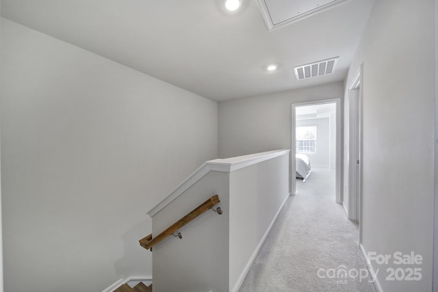 hallway featuring visible vents, baseboards, attic access, an upstairs landing, and carpet flooring