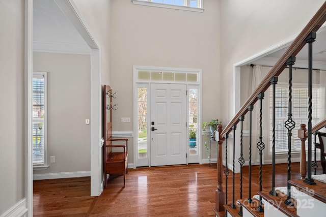 foyer with a wealth of natural light, stairs, a towering ceiling, and wood finished floors
