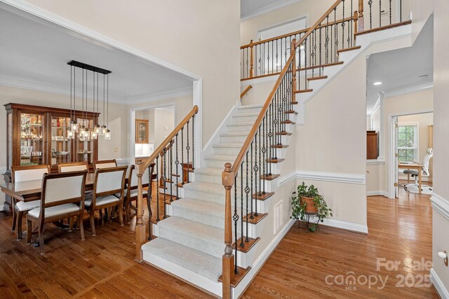 staircase with a high ceiling, wood finished floors, baseboards, and ornamental molding