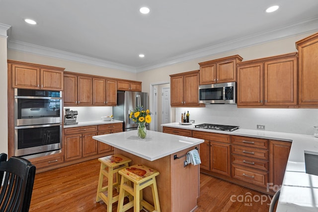 kitchen featuring light countertops, a kitchen island, brown cabinetry, appliances with stainless steel finishes, and wood finished floors