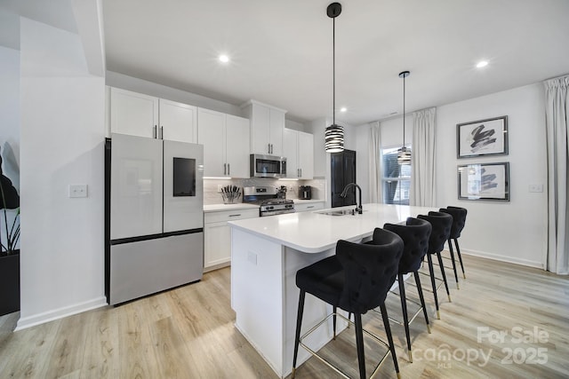 kitchen featuring a center island with sink, white cabinets, appliances with stainless steel finishes, a breakfast bar area, and backsplash