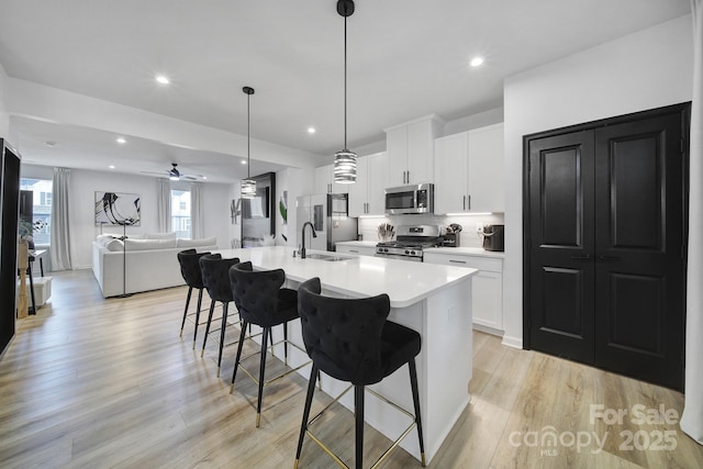 kitchen featuring stainless steel appliances, open floor plan, white cabinets, a sink, and a kitchen breakfast bar