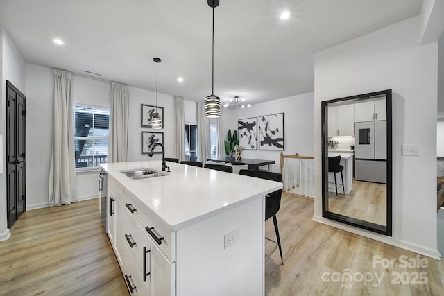 kitchen with built in fridge, a breakfast bar, light wood finished floors, white cabinetry, and a sink