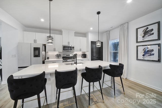 kitchen featuring a sink, light countertops, appliances with stainless steel finishes, backsplash, and a center island with sink