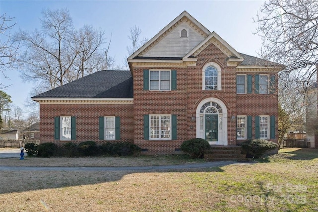 colonial home featuring a shingled roof, a front yard, crawl space, and brick siding