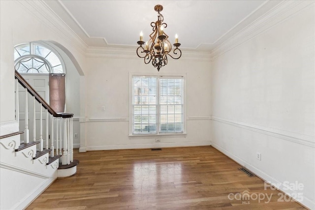 unfurnished dining area with arched walkways, stairway, ornamental molding, wood finished floors, and baseboards