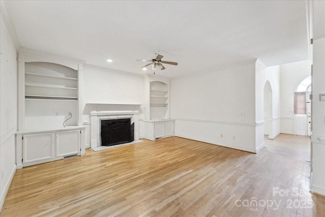 unfurnished living room featuring ceiling fan, light wood-type flooring, built in shelves, and a fireplace