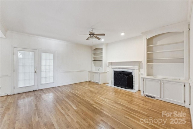 unfurnished living room featuring built in shelves, light wood finished floors, visible vents, a fireplace with flush hearth, and ceiling fan