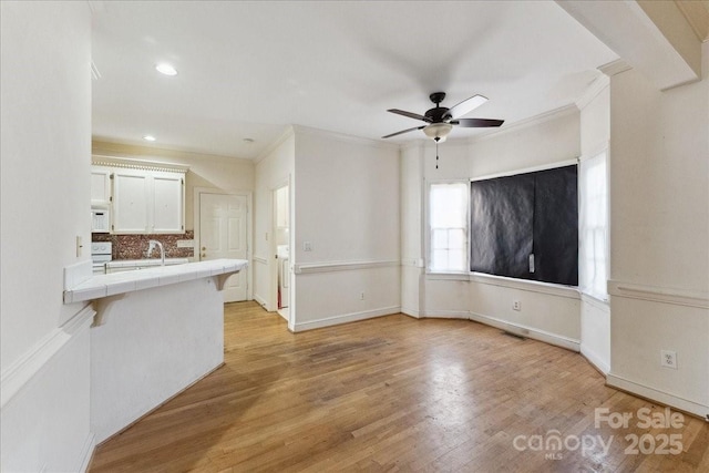 unfurnished living room featuring a sink, a ceiling fan, baseboards, light wood-type flooring, and crown molding