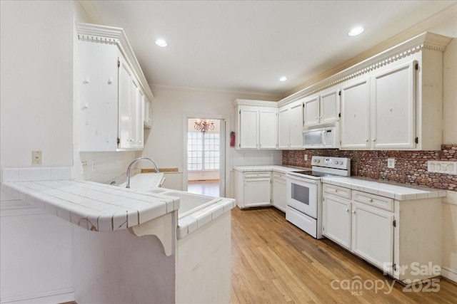 kitchen featuring tile countertops, a peninsula, white appliances, and light wood-type flooring