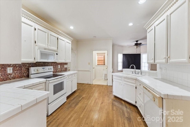 kitchen with tile counters, white cabinets, a sink, white appliances, and a peninsula