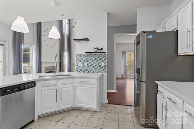 kitchen with decorative light fixtures, a sink, appliances with stainless steel finishes, white cabinets, and light tile patterned floors