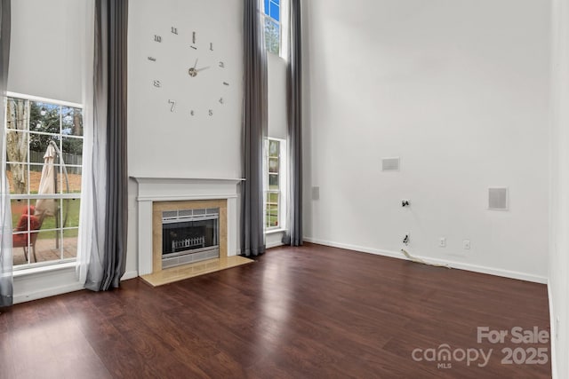 unfurnished living room with a tiled fireplace, wood finished floors, baseboards, and a towering ceiling