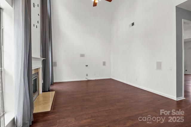 unfurnished living room featuring a premium fireplace, visible vents, ceiling fan, and dark wood-style flooring