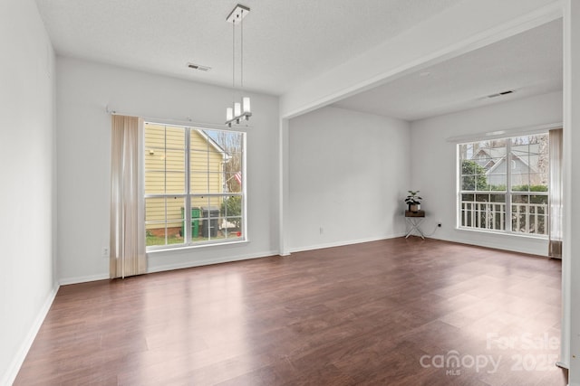 empty room with dark wood-style floors, baseboards, visible vents, a textured ceiling, and a notable chandelier