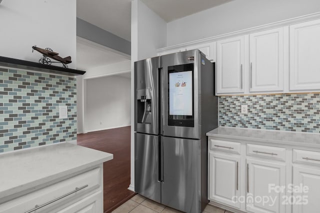 kitchen featuring white cabinetry, light tile patterned floors, stainless steel fridge, and backsplash