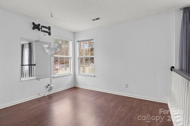 spare room with baseboards, wood finished floors, visible vents, and a textured ceiling