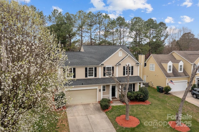 traditional home featuring driveway, a shingled roof, a front yard, an attached garage, and a chimney