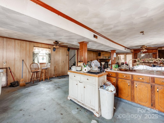 kitchen with a ceiling fan, light countertops, white cabinets, wood walls, and brown cabinets