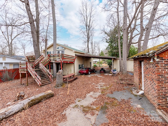 rear view of house featuring an attached carport, brick siding, a deck, and stairs