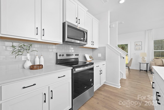 kitchen with stainless steel appliances, light countertops, light wood-style flooring, backsplash, and white cabinetry