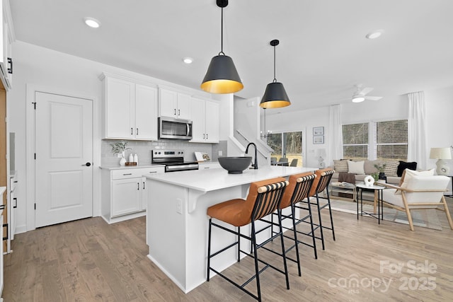 kitchen with a breakfast bar area, decorative backsplash, appliances with stainless steel finishes, open floor plan, and light wood-type flooring