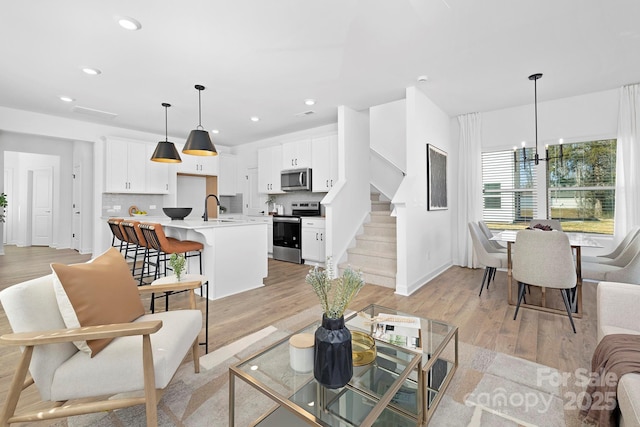 living area with baseboards, stairway, light wood-style floors, a chandelier, and recessed lighting