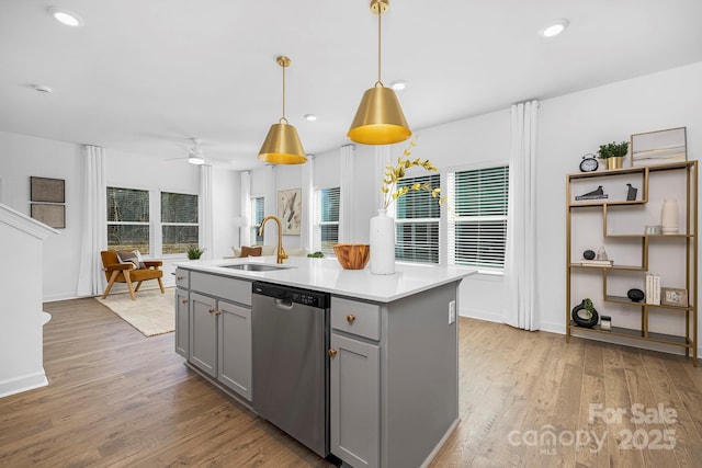kitchen with stainless steel dishwasher, light wood-style flooring, a sink, gray cabinets, and light countertops
