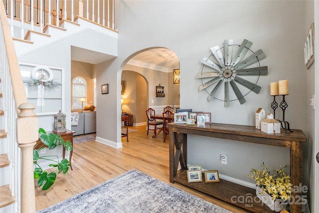 entryway with baseboards, arched walkways, a towering ceiling, ornamental molding, and wood finished floors